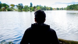 Symbolbild: Rückansicht eines Manns der auf einen See blickt.