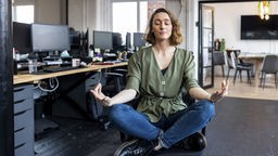 Eine Frau sitzt meditierend auf einem Bürostuhl