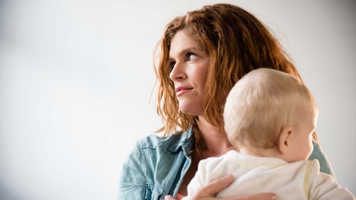 Symbolbild: Eine nicht glücklich schauende Frau hält ein Baby im Arm.