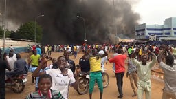 Während im Hintergrund das Hauptquartier der Regierungspartei brennt, demonstrieren Anhänger:innen putschender Militärs in Niamey, Niger (27.07.2023)