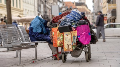 Obdachloser mit seinen Habseligkeiten in der Innenstadt auf einer Bank.