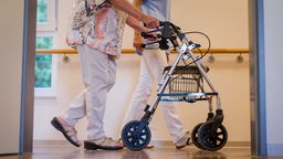 Symbolbild: Eine Pflegekraft begleitet einen älteren Menschen mit Rollator.