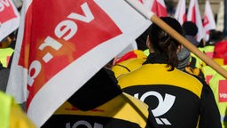 Menschen in Post-Uniform und mit Verdi-Fahnen beteiligen sich in Dortmund an einer Kundgebung anlässlich der Tarifverhandlungen (07.02.2023)