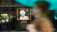 Eine Frau geht an einem Schaufenster vorbei, in dem ein Porträt von Elizabeth II. aufgestellt ist (London, 13.09.2022)