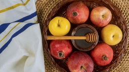 Äpfel und Granatäpfel in einem Korb, in ihrer Mitte ein Glas Honig