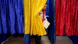 Eine Frau verlässt eine Wahlkabine, deren Vorhang die Farben der rumänischen Nationalflagge hat. Archivbild: 01.12.2024 - Parlamentswahl in Rumänien 