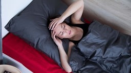 Symbolbild: Ein junger Mensch liegt im Bett und hält sich den Kopf