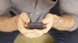Mann hält ein Smartphone in seinen Händen. Symbolbild