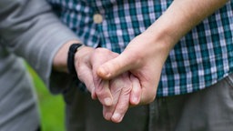 Symbolbild: Hand eines jüngeren Menschen, der die Hand eines älteren Menschen beim Gehen hält.