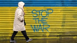 Frau Geht an einem Graffiti mit den Farben der Ukraine und dem Schriftzug STOP THE WAR vorbei. Symbolbild