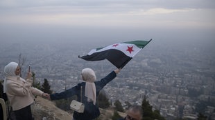 Eine Frau mit der Flagge der syrischen Opposition oberhalb der Stadt Damaskus. Symbolbild