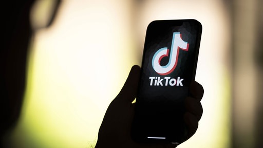 Eine Person hält ein Smartphone in den Händen, auf dem das Logo von TikTok zu sehen ist. Symbolbild