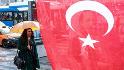 Frau mit Regenschirm läuft an einer türkischen Fahne vorbei. Symbolbild