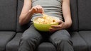 Ein Mensch sitzt auf einem Sofa mit einer Schüssel Chips.