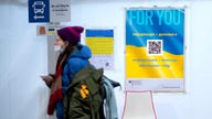 Geflüchtete aus der Ukraine vor einem Informations-Schild für Flüchlinge mit QR-Code