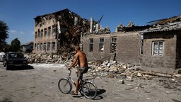 Ein Mann fährt Fahrrad in der Nähe einer zerstörten Schule in Torets (Ukraine, 22.08.2022)