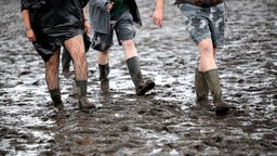 Menschen mit Gummistiefeln gehen in Wacken über das schlammige Festivalgelände.
