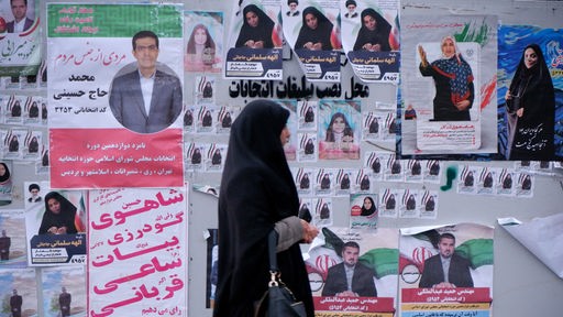 Eine verschleierte Frau in einem schwarzen Tschador geht neben den Wahlplakaten der Kandidaten für die bevorstehenden Parlamentswahlen im Iran entlang.