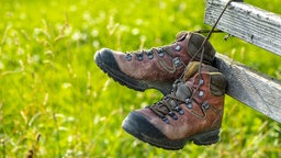 Wanderschuhe hängen über der Lehne einer Holzbank. Symbolbild