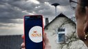 Symbolbild: Ein Mensch mit der Warn-App Nina auf dem Smartphone steht vor einem Haus mit Sirene auf dem Dach.