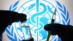 Silhouette von Händen in medizinischen Handschuhen, die eine medizinische Spritze und ein Fläschchen vor dem Logo der Weltgesundheitsorganisation (WHO) halten. Symbolbild