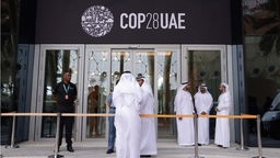 Menschen vor dem Eingang zu einem Konferenzgebäude mit dem Logo der COP28 (29.11.2023).