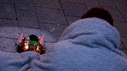 Ein Mensch hat eine Decke umhängen und bittet mit einer weihnachtlich geschmückten Dose um Spenden (2020)