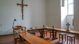 Innenraum der Abtei Mariawald mit Tischen mit Krügen und einem großen Holzkreuz an der Wand