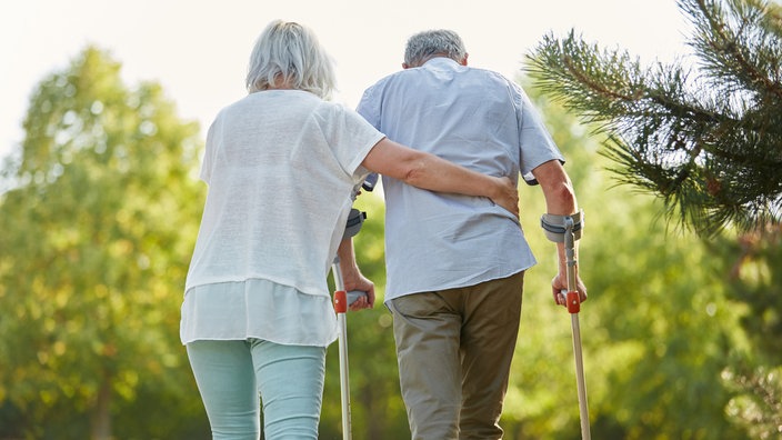 Eine Frau stützt einen Senior, der an Krücken geht