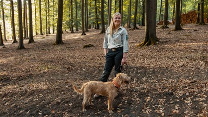 Anna-Maria Hille steht im Wald und hält einen Hund an der Leine