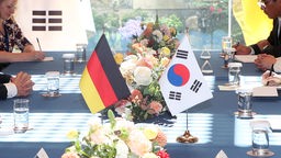 Politische Vertreter Deutschlands und Südkoreas sitzen am geinsamen Tisch - im Hintergrund die Flaggen beider Länder.