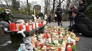 Menschen trauern an einer provisorischen Gedenkstätte mit Kerzen und Blumen für die Opfer des Messerangriffs in Aschaffenburg.