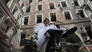 Im Innenhof eines zerstörten Hauses in Charkiw trägt ein Bräutigam seine Braut in den Armen 