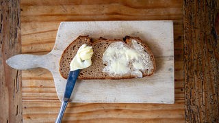 Eine Scheibe Brot mit Butter und einem Messer auf einem Holzbrett