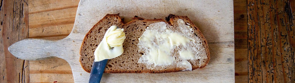 Eine Scheibe Brot mit Butter und einem Messer auf einem Holzbrett