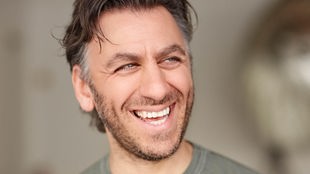 Der Schauspieler und Comedian Cem Ali Gültekin lacht auf einem Porträt