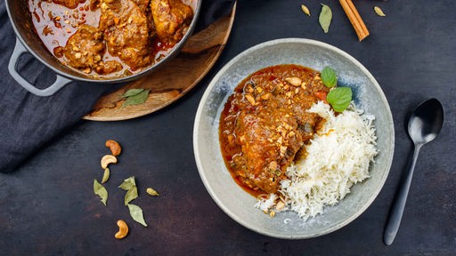 Ein Teller mit Chicken Korma und Reis, daneben eine Pfanne