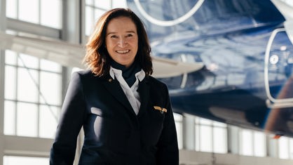 Porträtaufnahme von Cordula Pflaum in ihrer Pilotenuniform vor einem Flugzeug in einem Hangar.