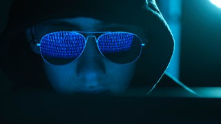Symbolbild Cybercrime: In der Sonnenbrille eines Mannes spiegeln sich binäre Zeichen.