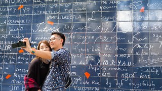 Touristen stehen und fotografieren sich im Stadtteil Montmartre in Paris (Frankreich) vor einer blauen Fliesenwand, auf der in allen Sprachen der Welt "Ich Liebe dich" steht.