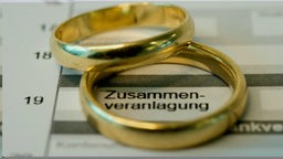 Zwei goldene Ringe liegen übereinander auf einem Steuerformular. Das Wort "Zusammenveranlagung" ist lesbar.