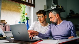 Ein Vater sitzt mit seinem Sohn an einem Laptop