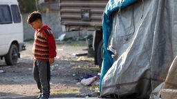 Ein Kind steht vor einer Notunterkunft aus Plastikplanen