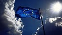 Fahne der Europäischen Union weht im Wind und wird von der Sonne angestrahlt. Gewitterwolken ziehen vorbei.