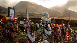 Blumenkränze und Blumen schmücken Kreuze an einer Gedenkstätte für die Opfer des Waldbrandes vom August oberhalb des Lahaina Bypass Highways.