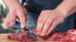 Die Händes eines Fleisch-Sommeliers mit Messer, der Fleisch zubereitet