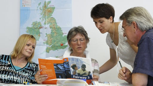 Erwachsene in einem Fremsprachenkurs lesen in einem Übungsbuch