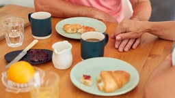 Symbolbild Probleme: Zwei Menschen halten Hand beim Frühstück.