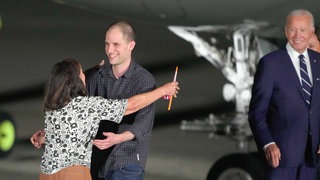 Der Reporter Evan Gershkovich (M) umarmt seine Mutter Ella Milman, während US-Präsident Joe Biden (r) zuschaut auf dem Luftwaffenstützpunkt Andrews nach dessen Freilassung im Rahmen eines Gefangenenaustauschs. 