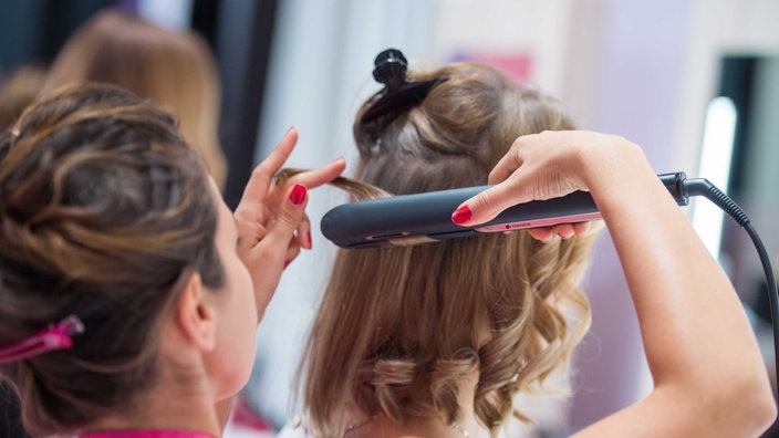 Einer Frau werden in einem Friseursalon die Haare geglättet. 